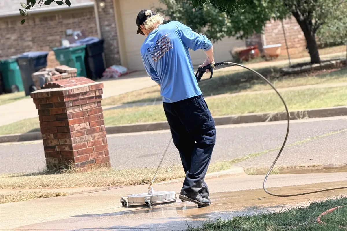 Brad running a surface cleaner across a concrete driveway at a brick home in the Oklahoma City metro